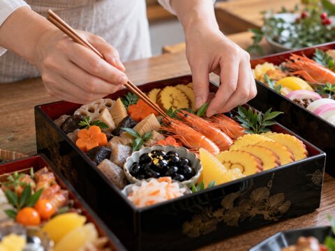 手作りのおせち料理を菜箸で漆塗りの重箱に丁寧に詰める、お正月の準備風景