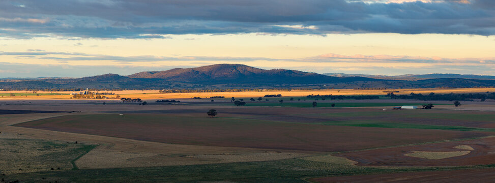 Aerial panorama view of a shaft of golden light over farmland between dry paddocks and distant hills