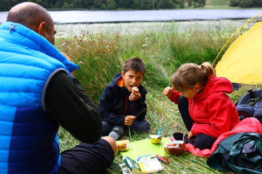 Family enjoys a picnic snack while camping outdoors by a lake