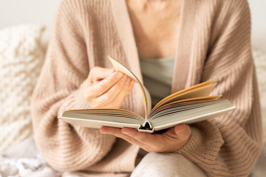 Woman reads book, turns page, and enjoys her leisure time indoors. Cozy moment of reading and self-education. Concept of slow and mindful living