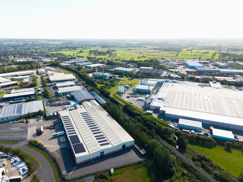 Aerial view of an industrial park featuring large warehouses with solar panels on the rooftops, surrounded by green fields and access roads in Lisburn, Northern Ireland, United Kingdom.