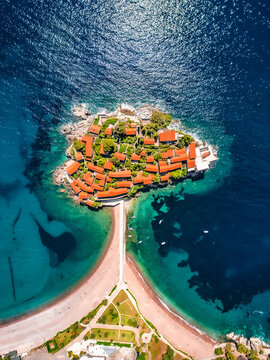 Aerial view of the historic island village of Sveti Stefan with red-tiled roofs connected to the mainland by a narrow causeway, surrounded by turquoise Adriatic waters in Sveti Stefan, Montenegro.