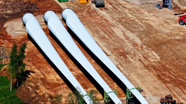 Aerial view of three large white wind turbine blades resting on the ground at a construction site in Latvia.
