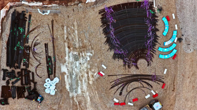 Aerial view of wind turbine foundation construction site with curved rebar segments and materials on gravel in Latvija.