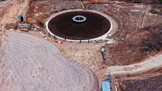 Aerial view of a wind turbine foundation under construction with a circular rebar structure on a dirt site in Latvia.