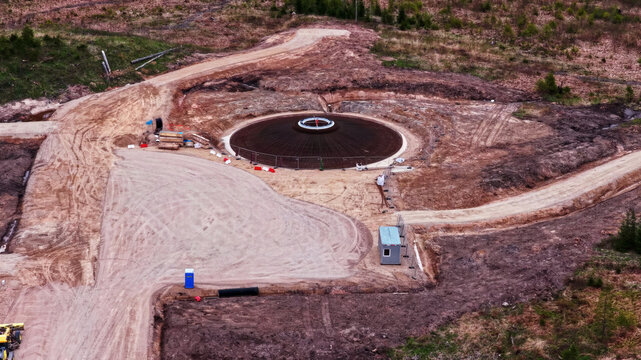 Aerial view of a wind turbine foundation under construction in a rural area with dirt access roads and site equipment in Latvia.