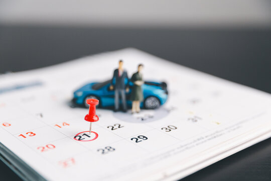 Miniature couple and toy car on calendar with pushpin marking a date, illustrating vehicle purchase appointment, family travel planning, rental booking, service reminder and payment deadline.