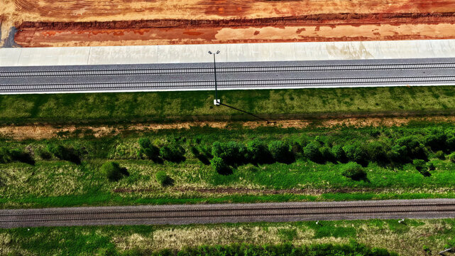 Aerial view of parallel railway tracks running through a green landscape with a construction zone and bare earth in Latvia.
