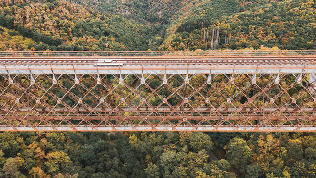 Aerial view of the historic Fades viaduct with its rusty metal truss structure spanning over a dense forest with autumn foliage in Les Ancizes-Comps, Auvergne-Rhone-Alpes, France.