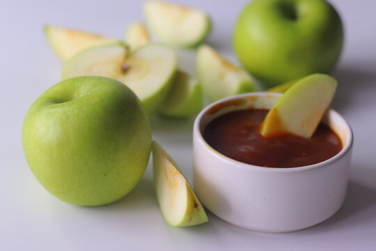 Green apples and sliced apple wedges served with smooth caramel dip on a clean white surface