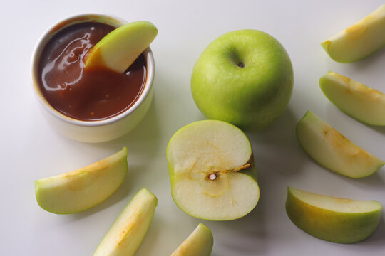 Green apples and sliced apple wedges served with smooth caramel dip on a clean white surface