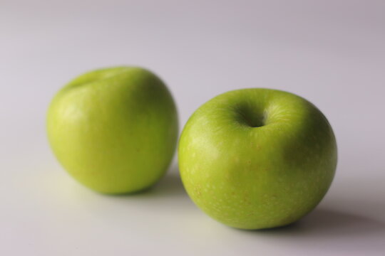 Two fresh green apples on a clean white surface with soft light and shallow depth of field