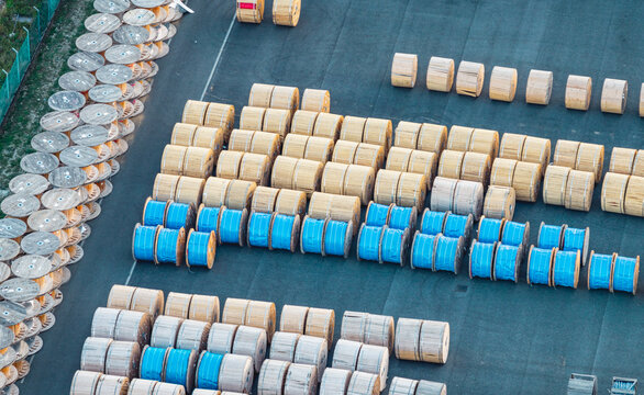Aerial view of wooden and blue-covered cable drums stored in organized rows at an industrial facility, highlighting logistics, manufacturing and electrical infrastructure. Italy.