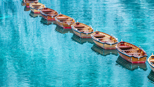 Aerial view of traditional wooden rowboats lined up on the turquoise water of Lago di Braies in the Dolomites, Italy.