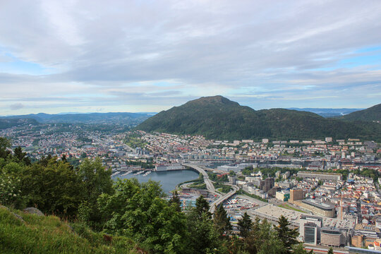European coastal city panorama and fjord tourism concept, aerial scenic view over waterfront city with bridge and harbor under mountains, representing travel destination, landscape, and port.