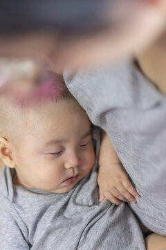Newborn peaceful sleep and infant care concept, sweet Asian baby boy sleeping gently in mother embrace in grey clothes, representing tender parenthood, pediatric health, and innocent dream.
