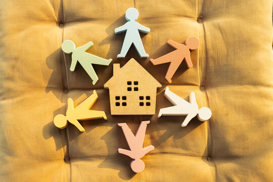Real estate community and family housing concept, colorful human figures gathered around wooden house model on cushion, symbolizing neighborhood unity, home insurance, and property loan.