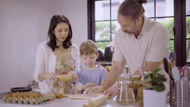 Caucasian family with parents teaching son kneading dough in kitchen
