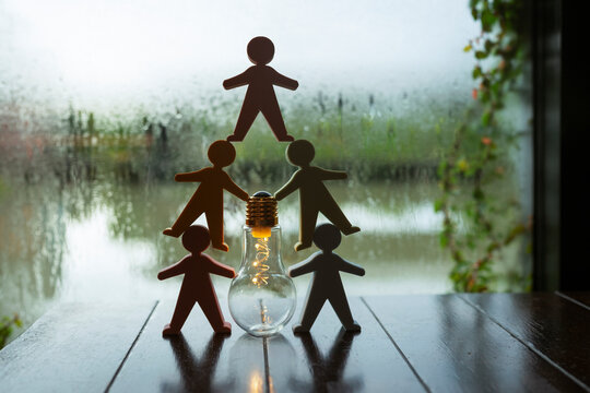 Team innovation and creative brainstorm concept, human figures stacked in pyramid around glowing light bulb on table, symbolizing collaborative idea, business solution, and startup energy.