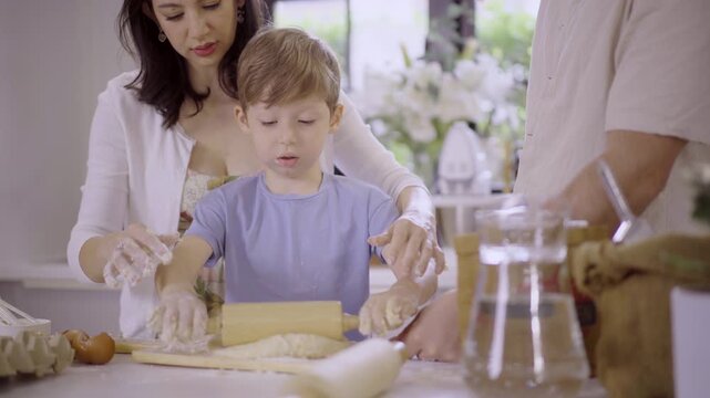 Caucasian family with parents teaching son kneading dough in kitchen