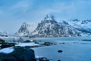 Majestic winter landscape of Lofoten Islands in Norway. Dramatic snow covered mountain peak towering over the cold sea fjord. Beautiful Arctic nature scenery of Scandinavian road trip vacation. © bank215