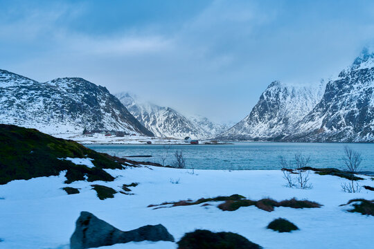 Remote winter coastal village nestled under majestic snow-covered mountains in Lofoten Islands, Northern Norway. Scenic Arctic fjord landscape during a Scandinavian road trip travel adventure.