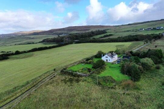 Aerial view of a white house nestled in the green fields of the Scottish countryside with rolling hills and a cloudy sky in Stein, Scotland, United Kingdom.