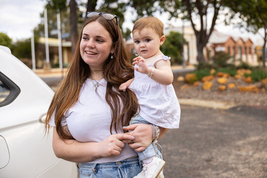 Smiling mother holding her little child outdoors near parked family car