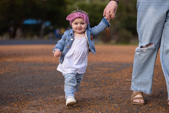 Toddler taking first steps while holding mother's hand outdoors