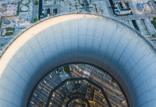 Aerial view of a massive concrete cooling tower at an industrial power plant, revealing its circular structure, support columns and dramatic engineering design in Italy.