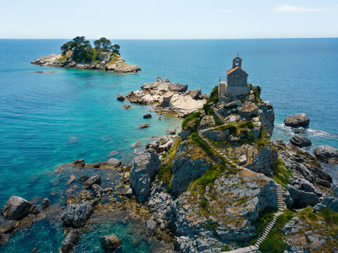 Aerial view of St. Nedjelja Church on a rocky islet surrounded by the clear blue Adriatic Sea with a second islet in the background, Petrovac, Montenegro.