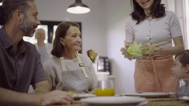 Woman serving fresh salad bowl to family members at dining table