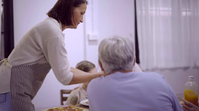 Woman serving fresh salad bowl to family members at dining table