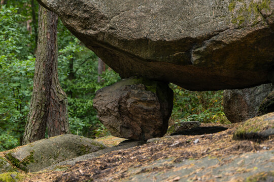 Massive balancing boulder resting on a smaller stone in a green forest, natural rock formation, precarious stability