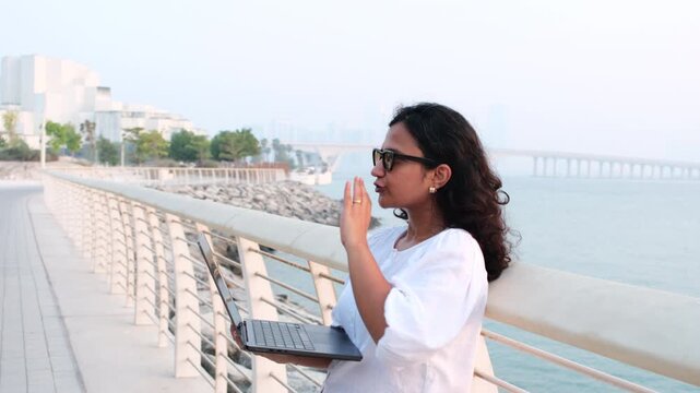 Remote working woman with laptop by Abu Dhabi waterfront for work from anywhere and digital nomad lifestyle