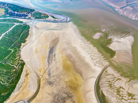 Aerial view of the Baie de Somme featuring intricate tidal sand patterns, winding water channels, and lush green salt marshes in Saint-Valery-sur-Somme, Hauts-de-France, France.