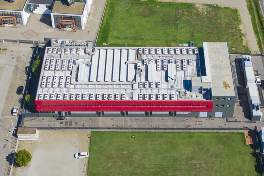 Aerial view of a modern datacenter building featuring a flat roof densely packed with numerous HVAC cooling units and a prominent red facade section, Arezzo, Tuscany, Italy.