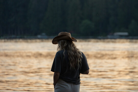 Woman in a hat watching a golden sunset over a lake