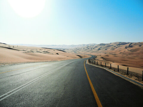 An empty highway curves through endless desert sand dunes
