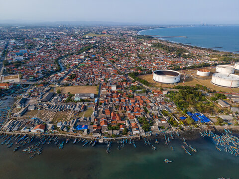 Aerial view of the coastal town of Cilacap Regency with harbor, fishing boats, residential area, and industrial oil storage tanks in Cilacap Regency, Central Java, Indonesia.