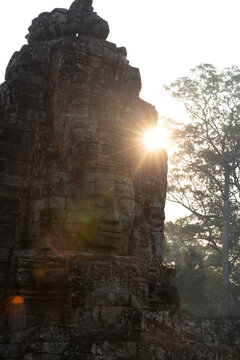 Sunrise flare behind ancient stone face at Bayon Temple
