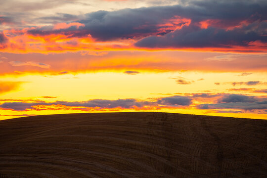 Fiery orange sunset clouds over a rolling farm hill