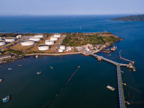 Aerial view of an oil terminal with large storage tanks, a long jetty extending into the sea, and small boats near the coast in Cilacap Regency, Central Java, Indonesia.
