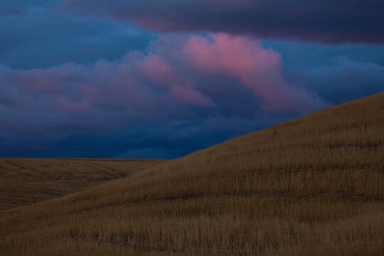 Dramatic pink clouds over rolling harvested hills at dusk