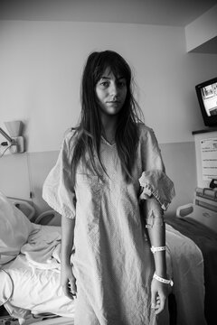 Young woman patient in gown standing in hospital room