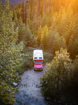Aerial view of a red truck camper in a forest at sunset