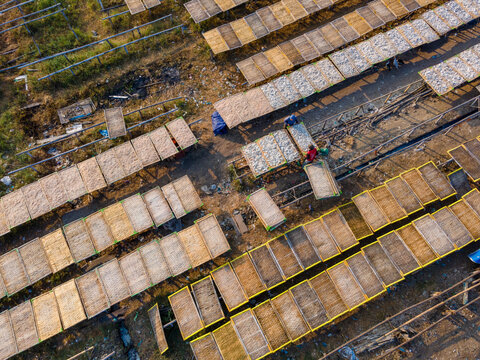 Aerial view of workers drying fish on bamboo racks in a traditional processing area in Cilacap Regency, Central Java, Indonesia.