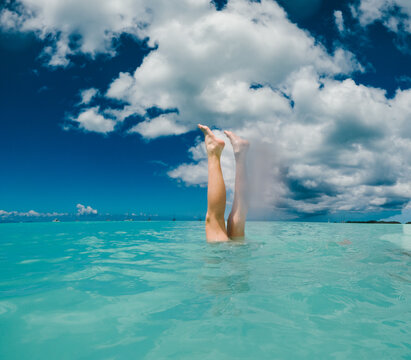 Person's legs sticking up from turquoise ocean water