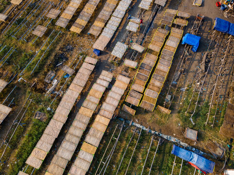 Aerial view of wooden racks used for drying fish in an open field, with workers tending to the catch and blue tarps in Cilacap Regency, Central Java, Indonesia.