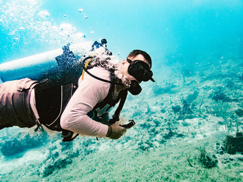 Male scuba diver swimming over a sandy seabed